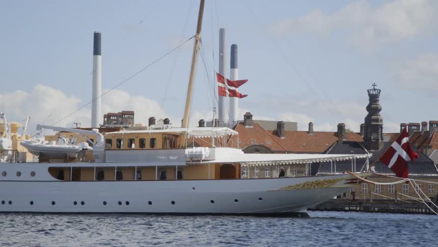 A ship waving a red and white flag moves past building on a dock