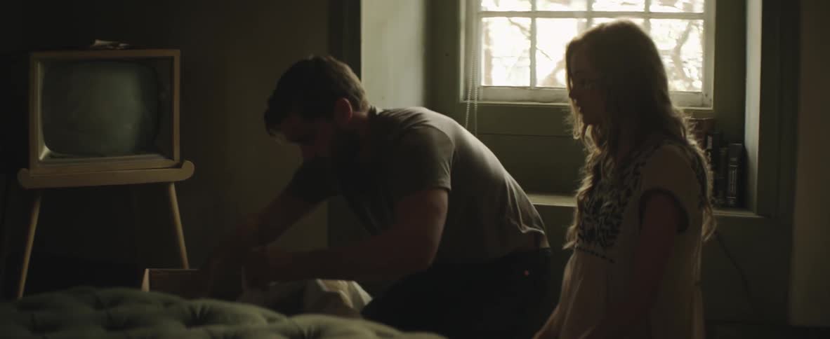 A man and woman go through a box of items in a living room