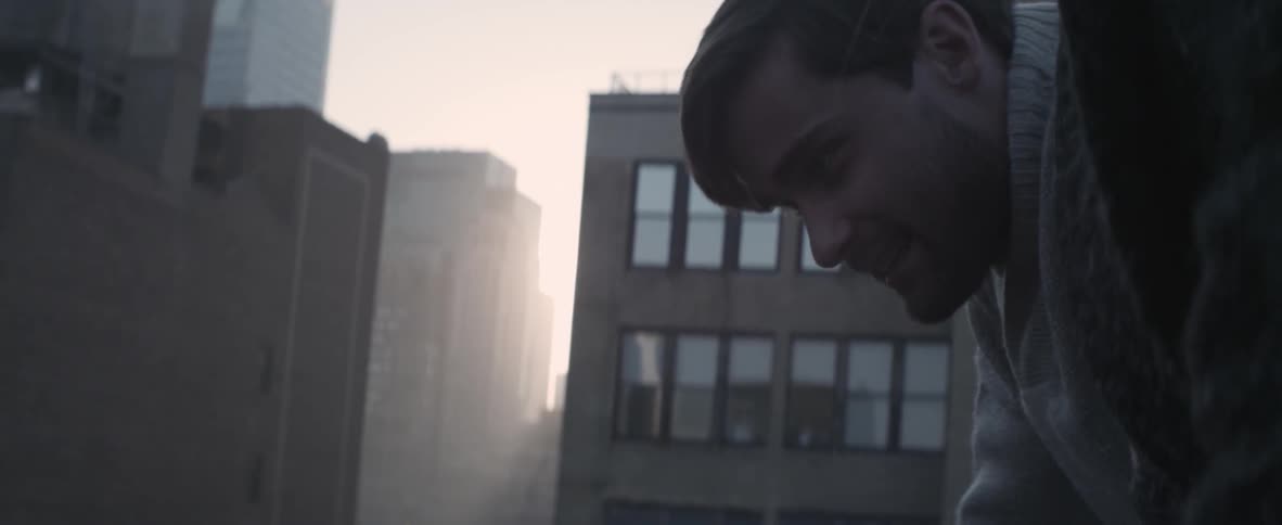 A man and woman talk in front of misty buildings