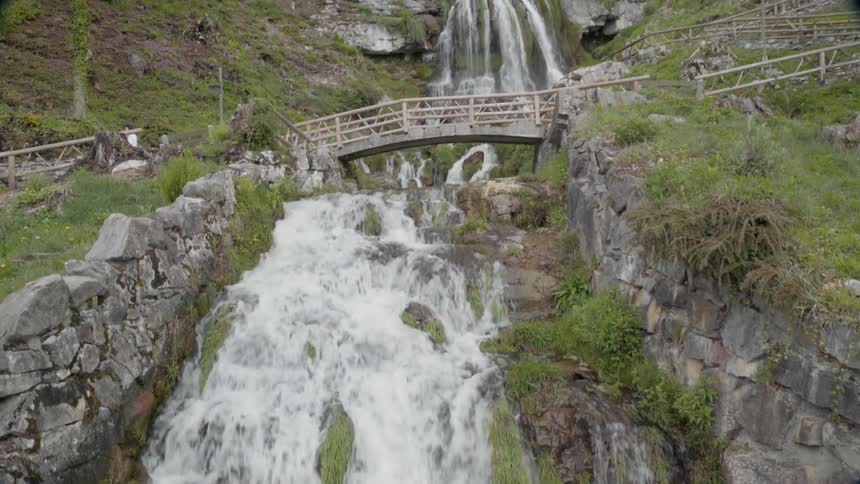 The waterfall rages as people cross over the bridge