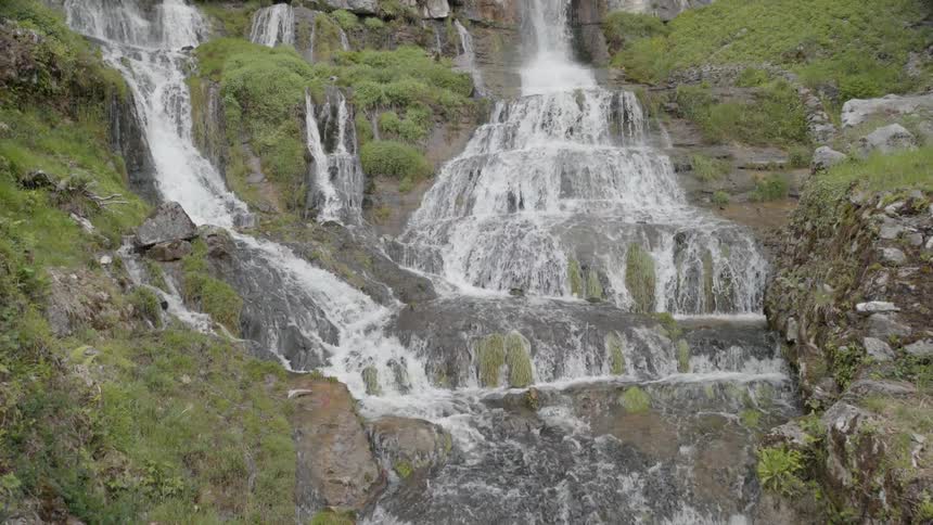 The wide waterfall is pouring all over the grass and rocks