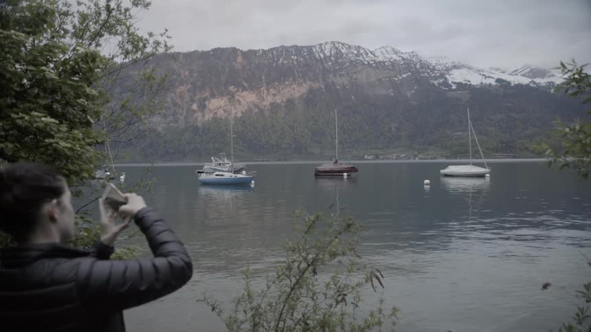 A woman taking a picture of boats on the water with her cellphone