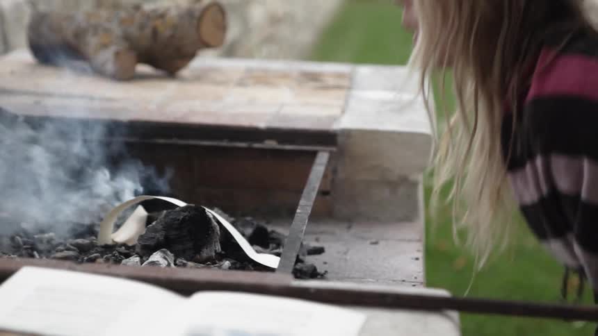 A woman adds paper to a fire and blows on it