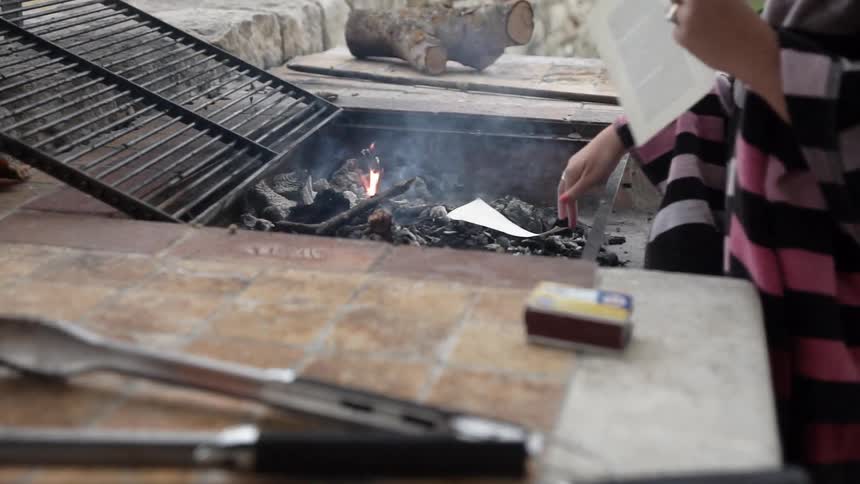 A person is adding paper to a fire in the yard