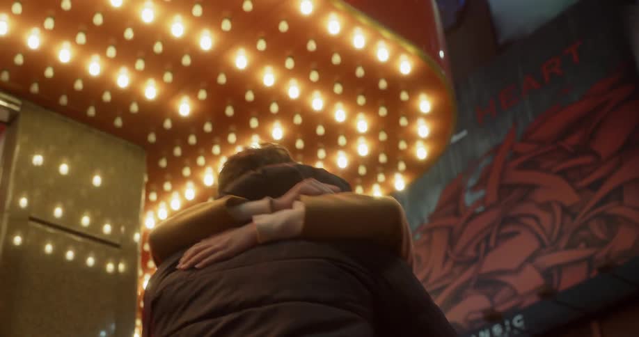 Man and woman hug under flashing bulb lights on a city sidewalk at night