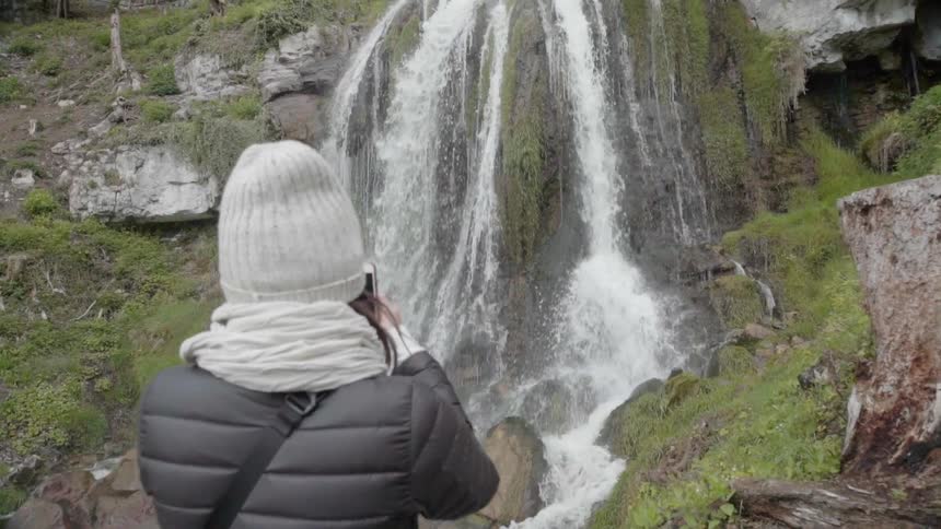 A woman photographs a waterfall with her phone