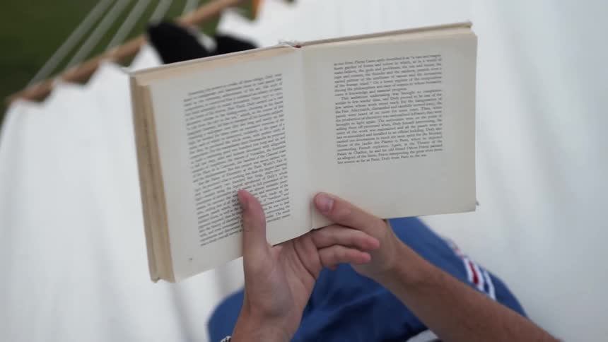 Person reads a book while sitting in a hammock