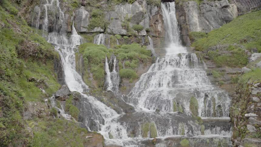 Water pours down a mossy rock formation with a small building on top