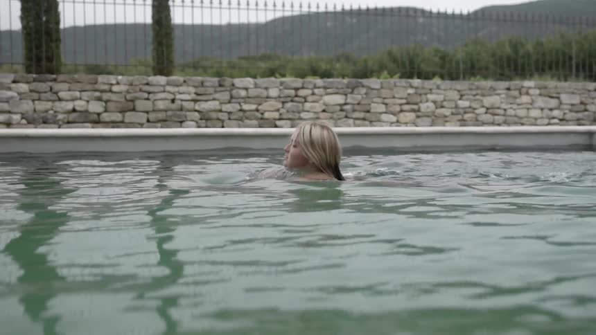 Woman swims in a pool near a fence