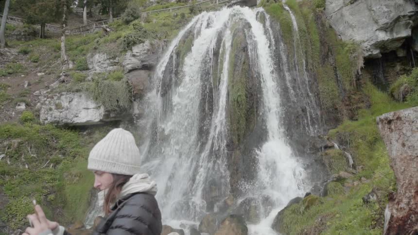 A woman takes a photograph by the waterfall