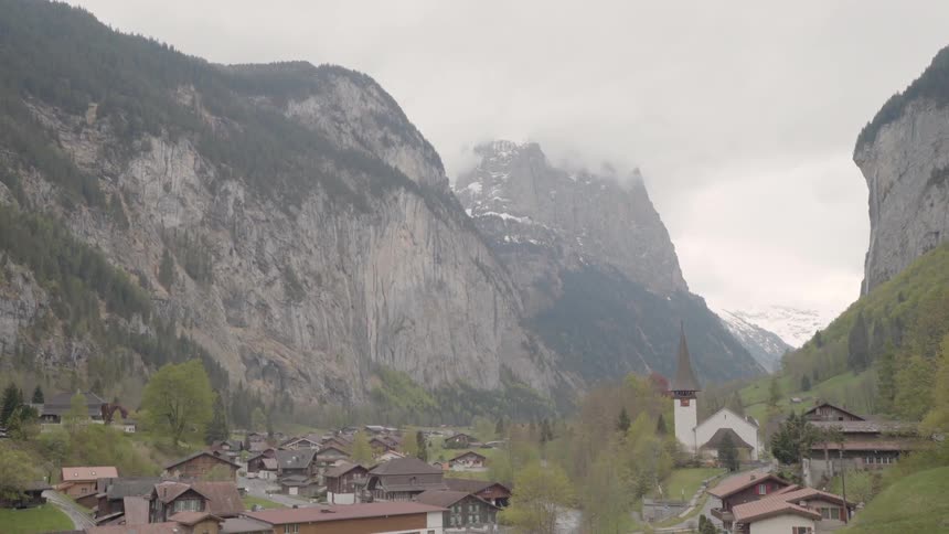 Clouds roll over tall rocky hills and a village below