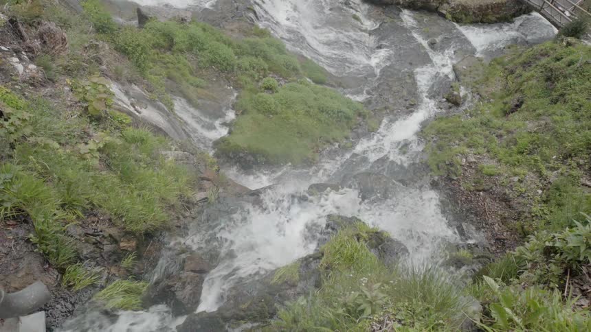 The water is rushing past the rocks and grass in the stream