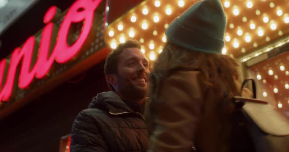 A man and woman hug on a city sidewalk at night