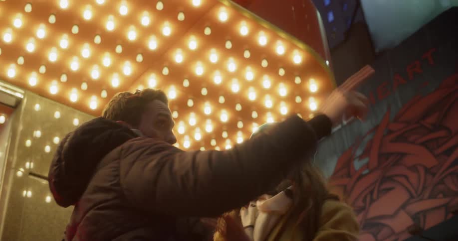 Man and woman smile and hug outside on a lit up city street