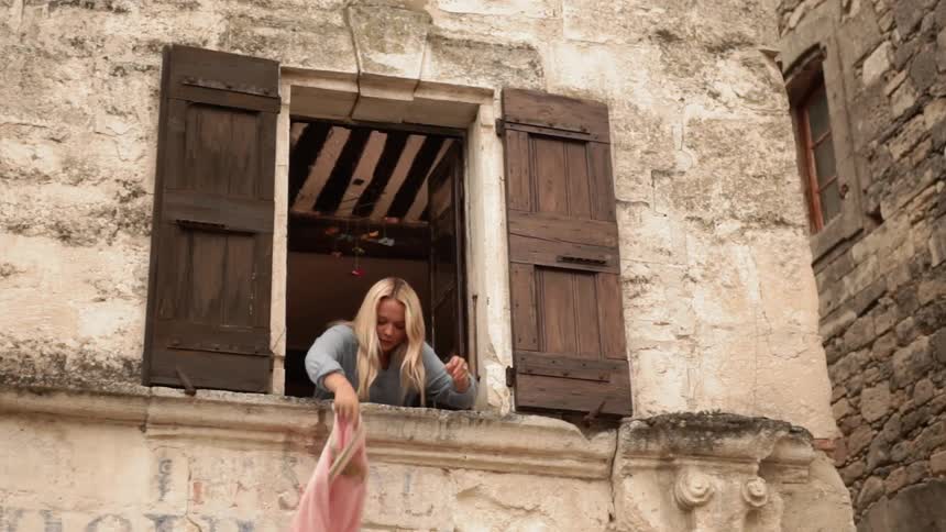 A woman shakes a blanket out the window