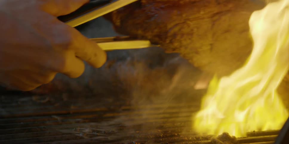 Person flips a steak over on a grill and fire flames up