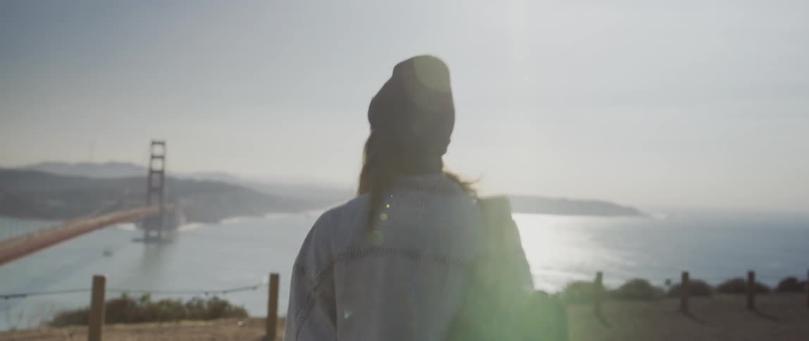 A woman is walking towards the water by the bridge