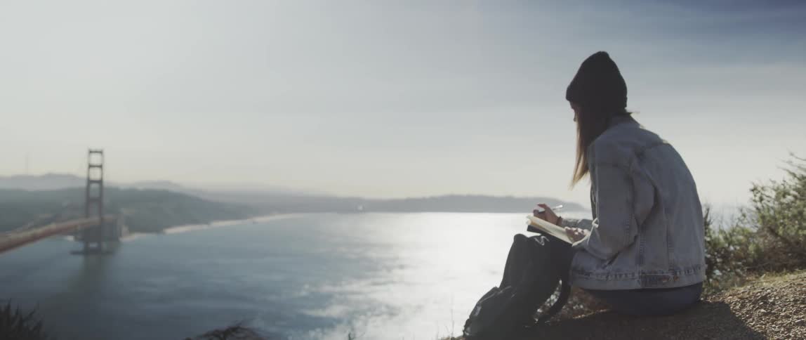 A woman writes in her notebook on the hill top