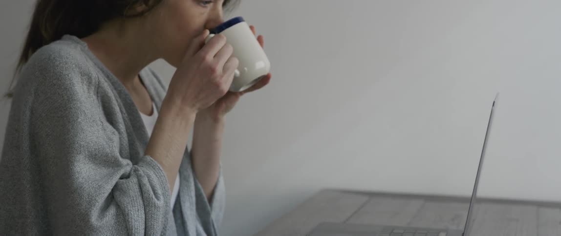 Woman drinks from a mug then types on a laptop