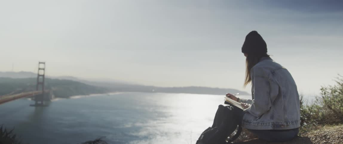 A woman sits on the cliff ledge overlooking the water