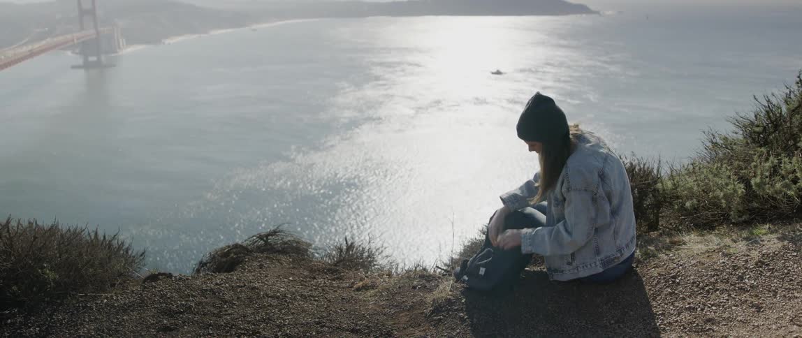 A woman puts some books into her backpack by the lake