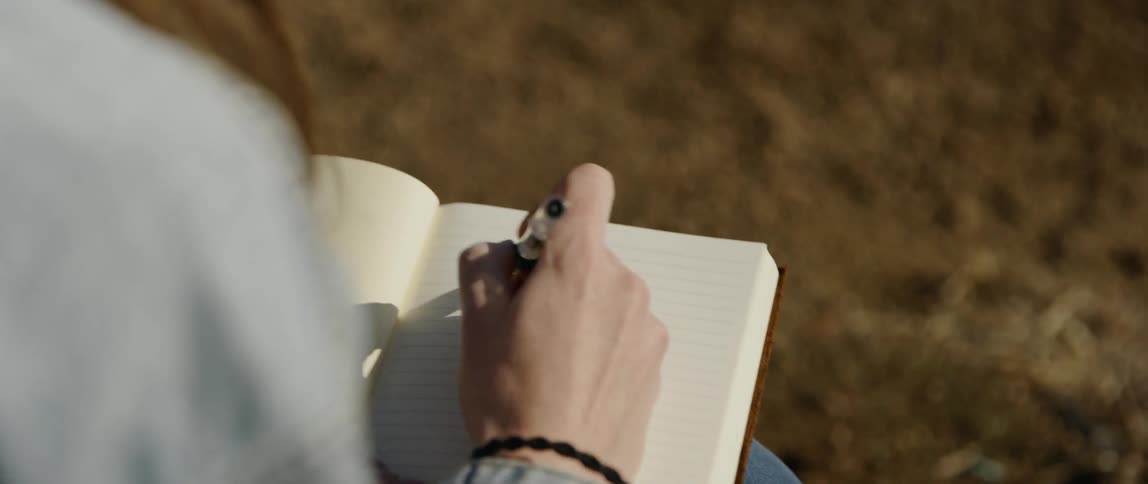 Woman writes in a notebook with a pen under the bright sun