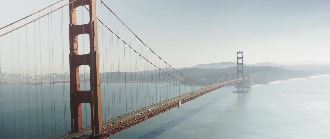 The cars travel over the bridge on a foggy day