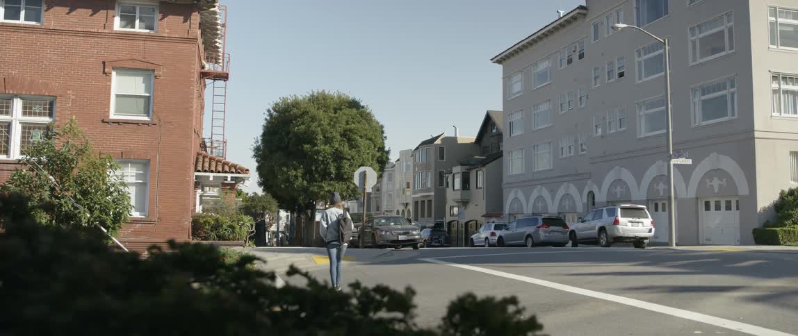A woman carrying a bag crosses a city street on a sunny day