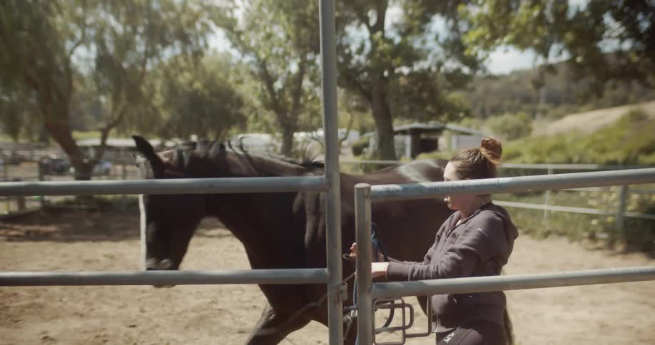 Woman removes a rope from a horse in a corral then it trots away