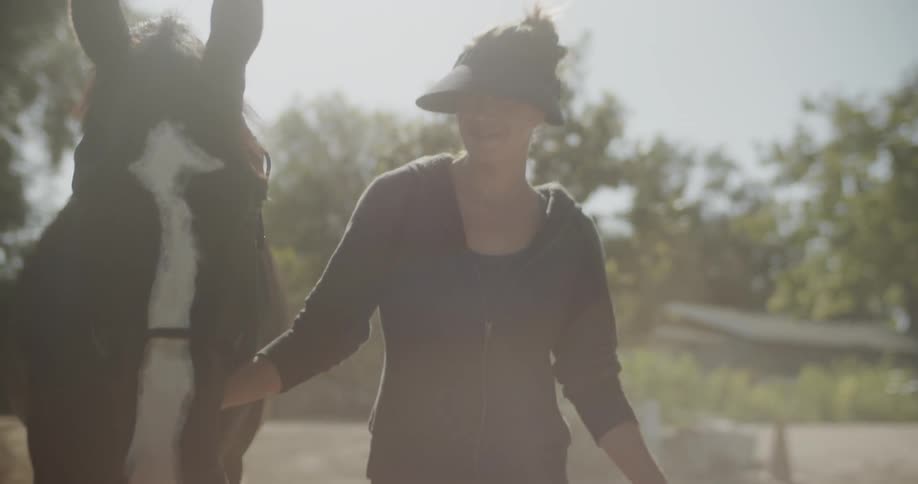 Woman holds onto a horse as she walks with it near the trees