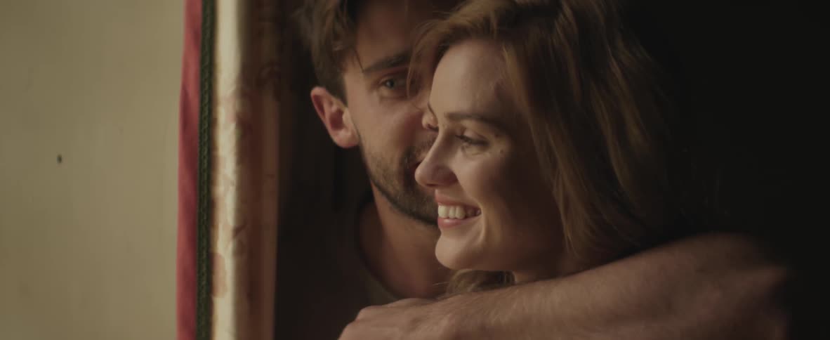 A man and a woman cuddle as they look at a window