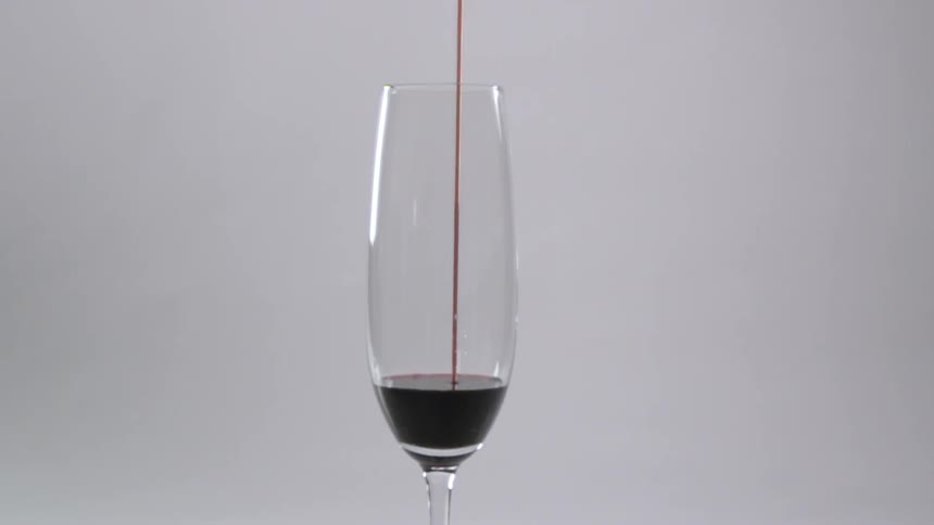 Red wine pours in a stream into a tall wine glass