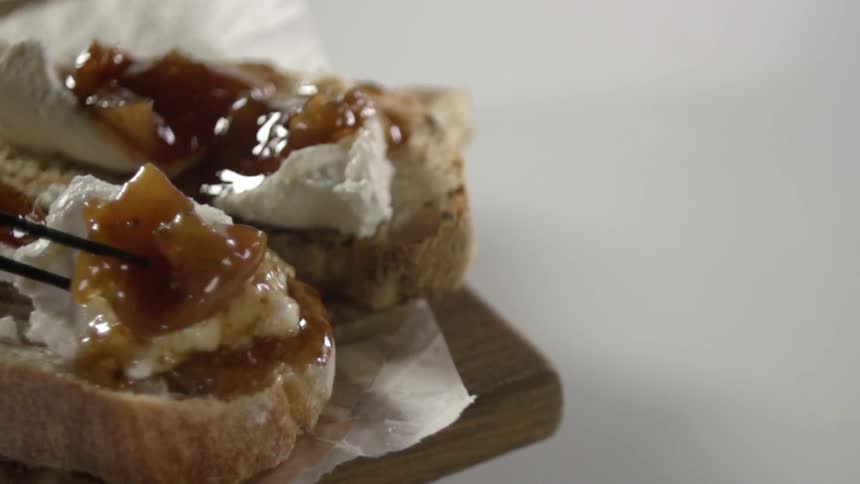 A piece of fruit is placed on bread using tongs