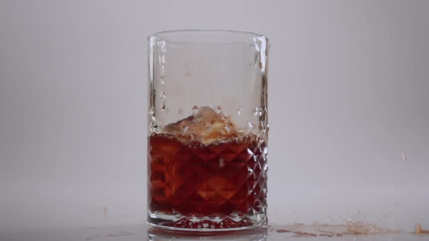 The ice cube falls in the glass splashing the beverage