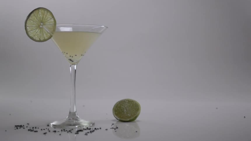 Black seeds are dropped into a cocktail in a martini glass