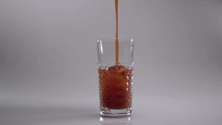 A brown liquid is poured into a clear glass with ice cubes in it