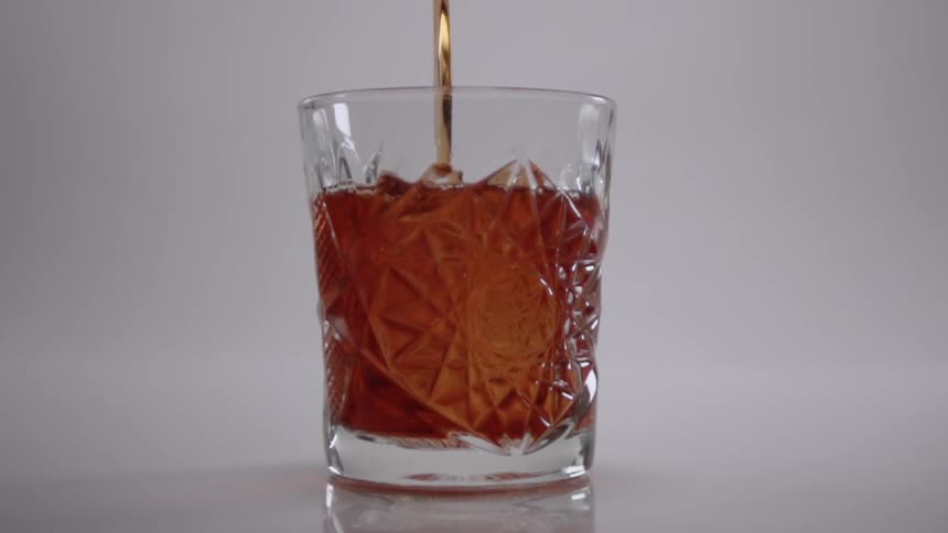 The small glass is being filled with a beverage