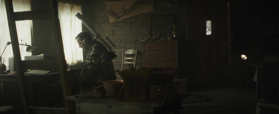 A man sits at a desk wearing headphones and talking, there is a telescope in the background