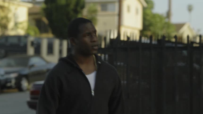 Man wearing a jacket moves quickly around the corner near a fence
