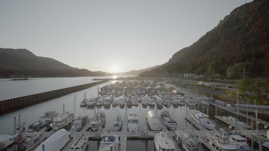 Slow pullback reveal of a quaint harbor as the setting sun reflects in calm water