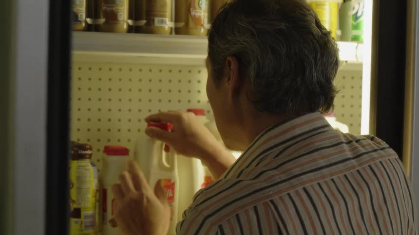 A man is checking the dates on milk in the fridge