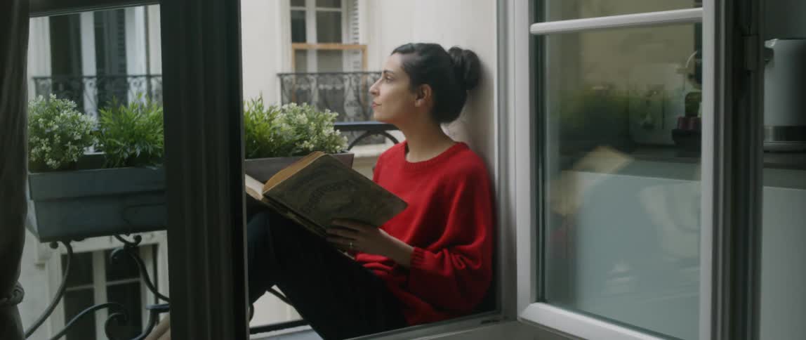 The woman looks out the window before looking back to her book