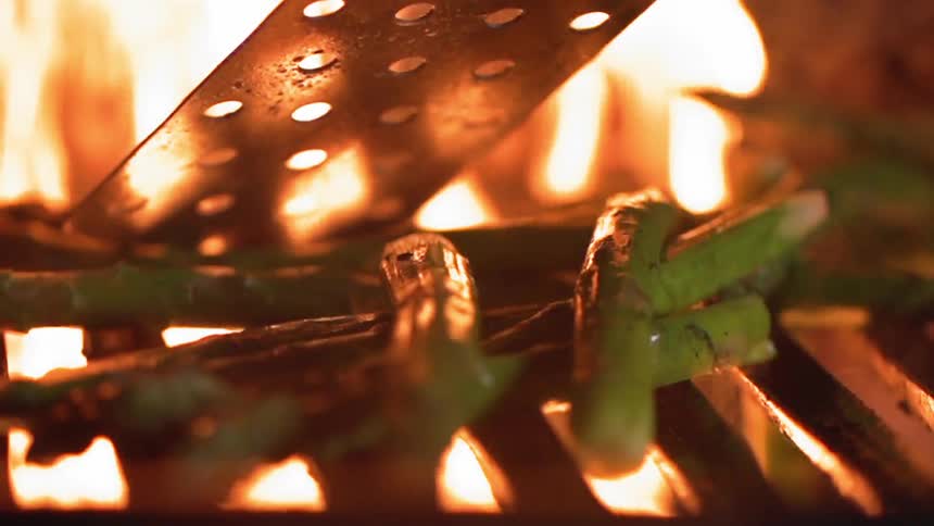 Asparagus spears are added to a flaming grill
