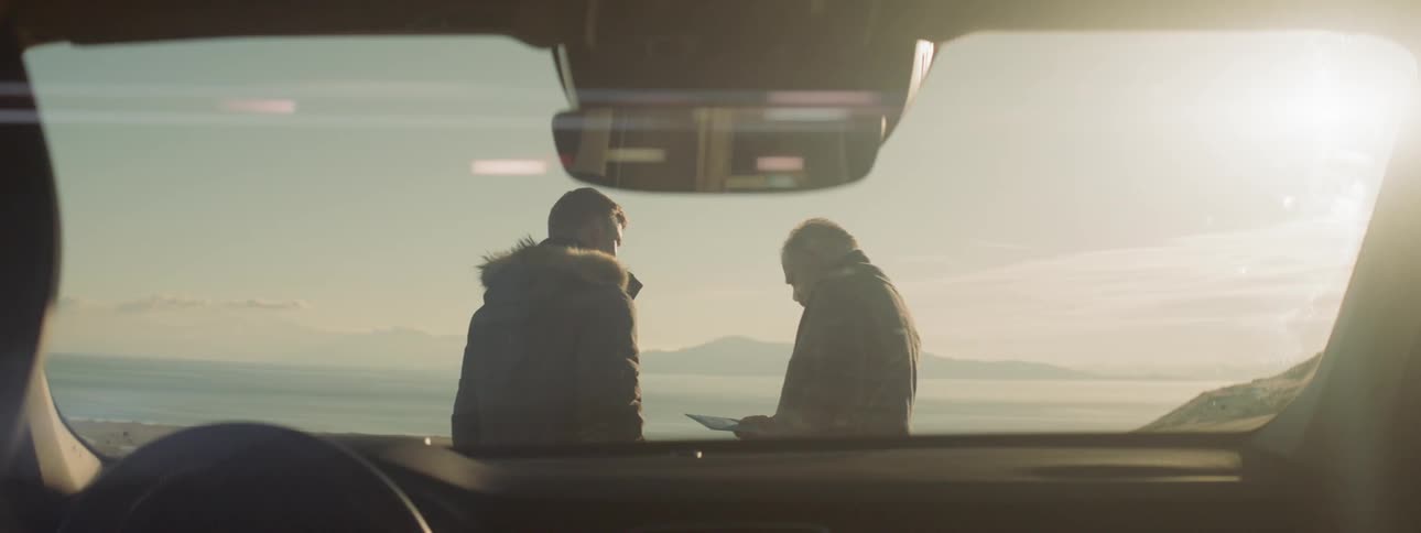 Two men talk in front of the car windshield