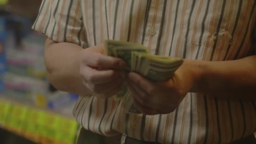 A man in a store counts and heads one dollar bills