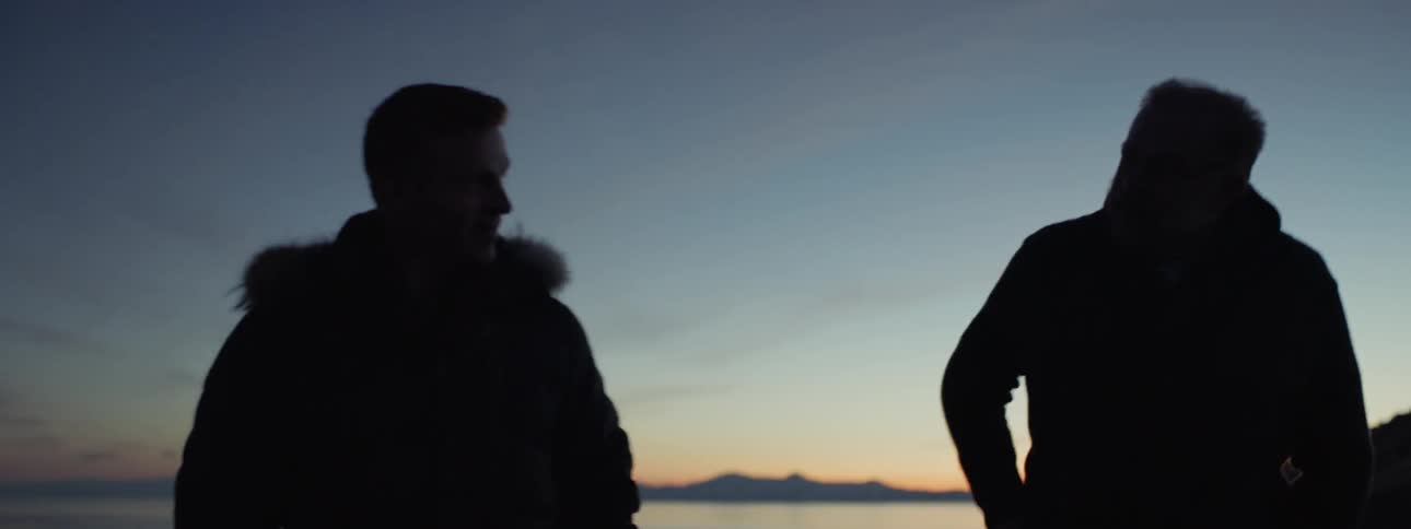 Two men walk near a mountain lake at dusk