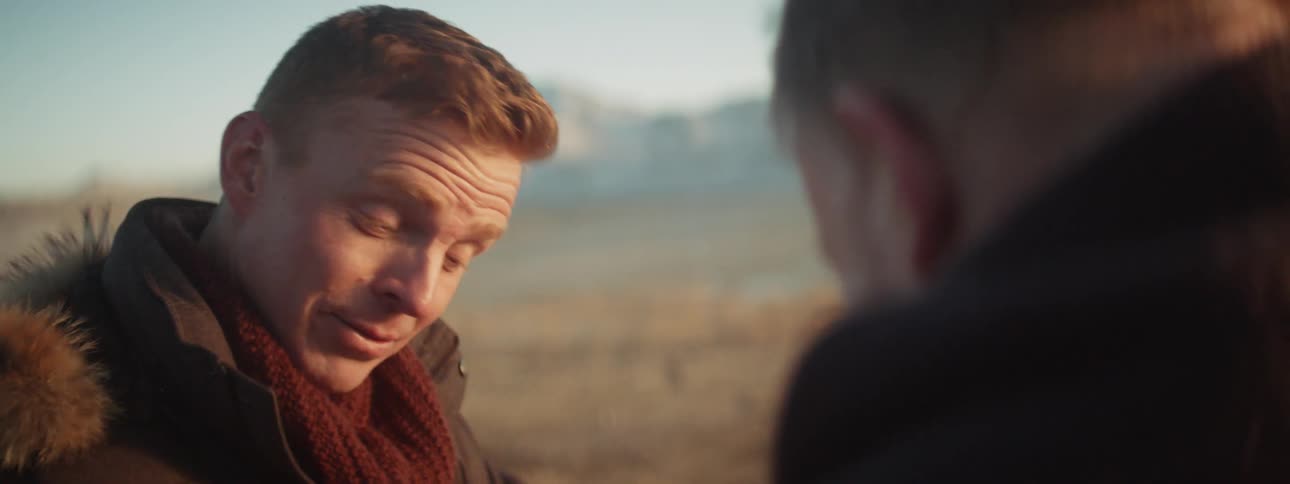 Two men talk near snowy mountains at sunset