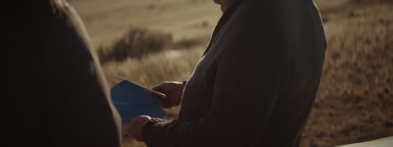 A man standing outside opens a card handed to him