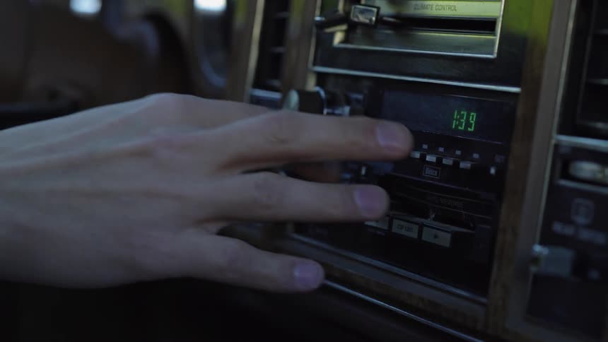 A person is tapping the buttons on a car radio as they drive in daylight