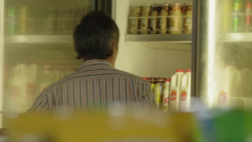 A man is closing the door of a cold case in a shop at night